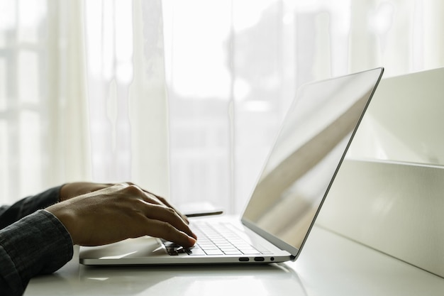 Le mani dell'uomo utilizzano il computer portatile con lo smartphone su un tavolo bianco a casa shopping online lavoro a casa freelance concetto di apprendimento online