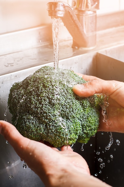 Man&#39;s hands washing broccoli. Water flows on broccoli. Ingredient for dietary breakfast. Make sure it&#39;s perfectly clean.