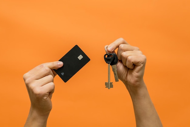 Мужские руки с ключами и кредитной картой изолированы на оранжевом фоне