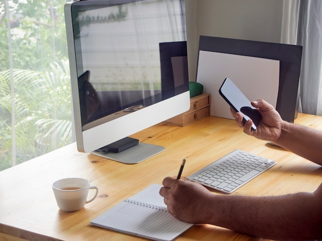 Man's holding phone on desk at home.