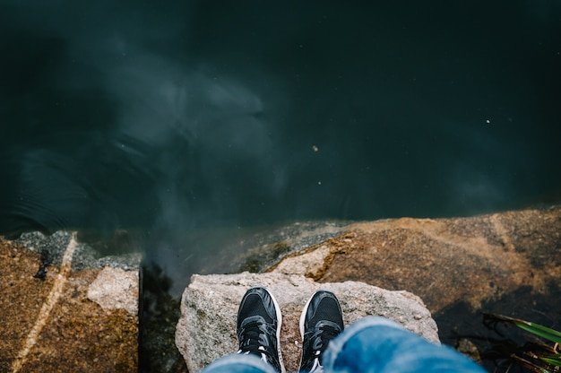 Man's legs stand on a stone in front of the lake