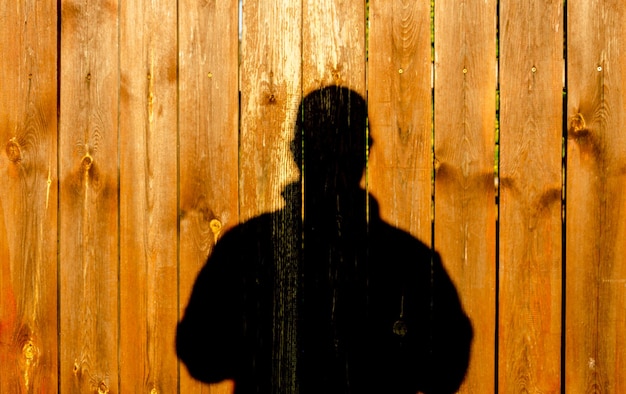 Photo a man's shadow on a wooden fence.