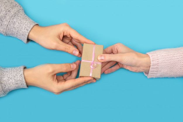 Man's and woman's hands keep box with gift on blue.