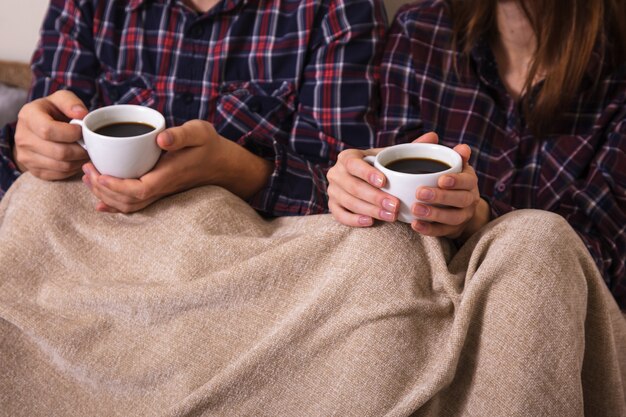 Man's and woman's hands keeps two cup of coffee in worm plaid.