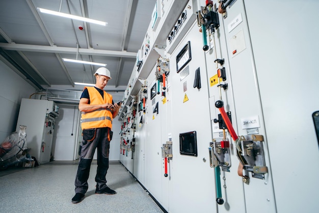 A man in a safety vest stands in a room with a control panel and a control panel.