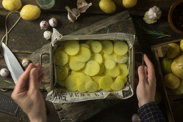 Man salt sliced potatoes for cooking on rustic wooden table