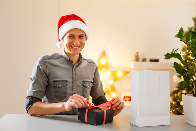 Uomo in cappello di babbo natale che tiene il computer portatile con buon natale digitando