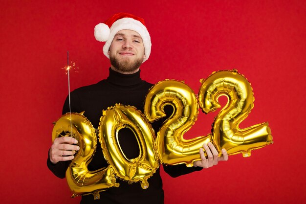 サンタクロースの帽子をかぶった男が2022年の数字と線香花火を持っています