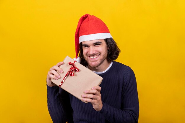 A man in a santa claus hat shows the christmas present a package with brown paper and red ribbon