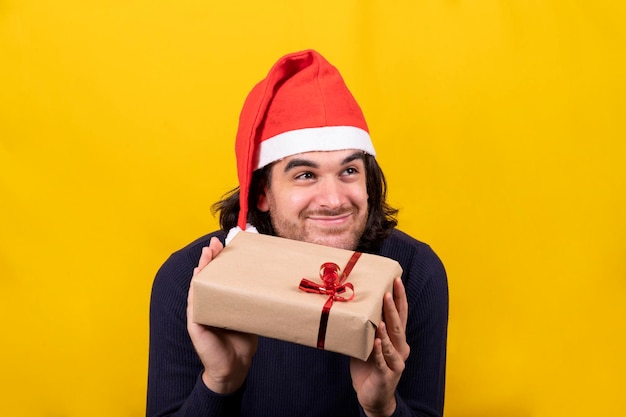 A man in a santa claus hat shows the christmas present a package with brown paper and red ribbon