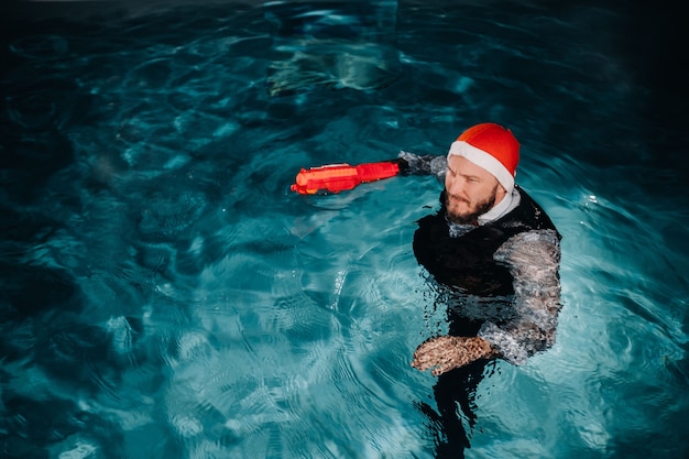 Un uomo vestito da babbo natale e cappello con una pistola rossa in mano. babbo natale sta nuotando sott'acqua con una pistola. concetto di natale