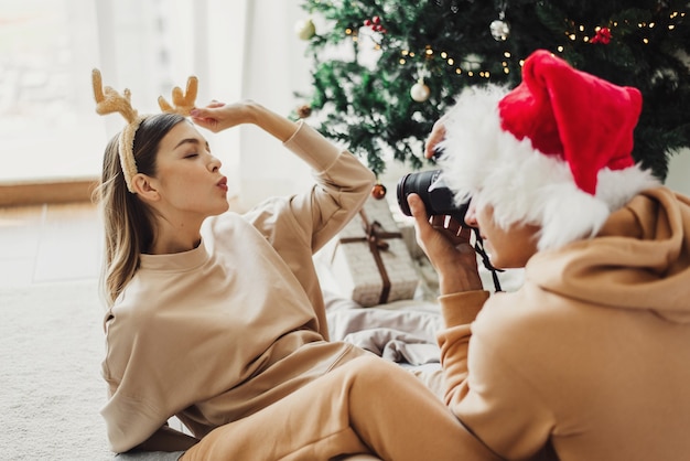 산타 모자를 쓴 남자가 장식용 크리스마스 사슴 핸드밴드를 착용한 젊은 여성의 사진을 찍고 있다