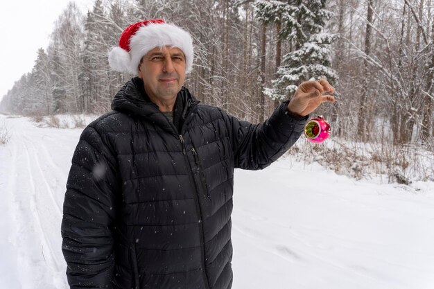 A man in a santa hat with a christmas ball in the winter in the forest person