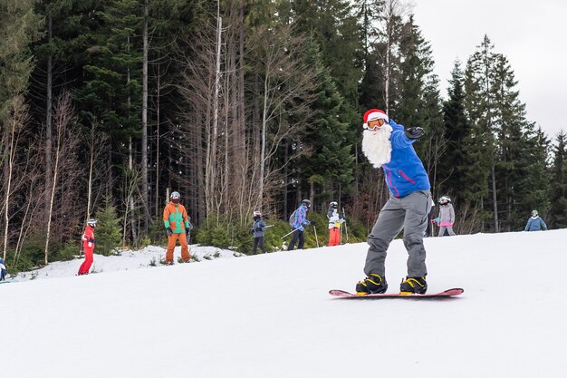 A man in a santa hat with a snowboard at a ski resort.