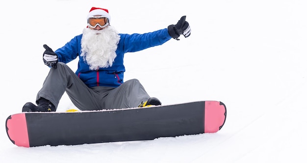 Un uomo con un cappello da babbo natale con uno snowboard in una stazione sciistica.