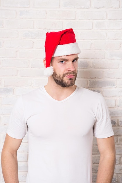 Man santa in tshirt op witte bakstenen muur. Man met baard op ernstig gezicht in rode kerstmuts. Kerstman mode. Kerst- en nieuwjaarsfeest. Vakantie viering concept.