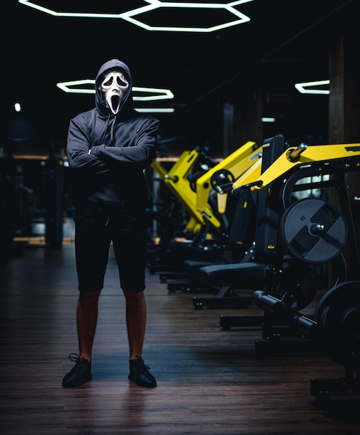 Man in scary mask in gym standing dark male person in halloween\
mask