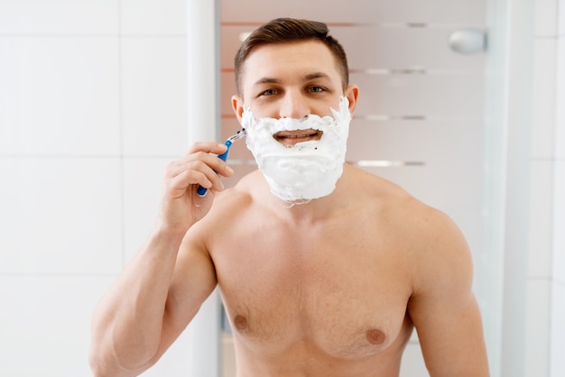 Man scheert zijn baard met een scheermesje in de badkamer, routine ochtendhygiëne.