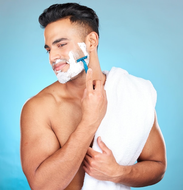 Man scheren gezicht en studio voor wellness huidverzorging en handdoek met geluk door blauwe achtergrond Model ontharing van het gezicht en cosmetisch schuim voor zelfzorg en schoonheid van de huid met cosmetica op achtergrond