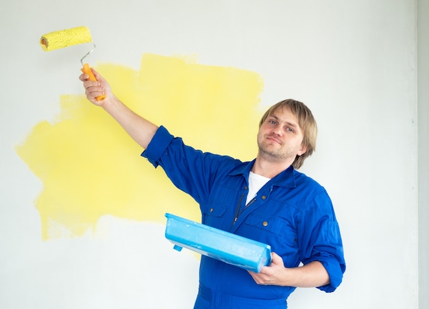 Man schilderij muur in gele kleur met roller. Renovatie, reparatie en herinrichting concept.