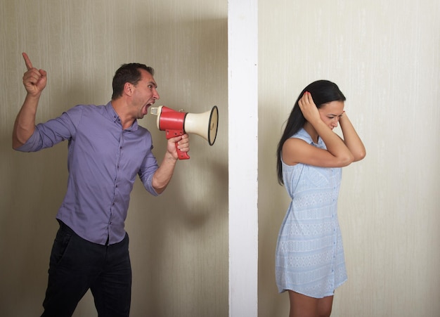 Man schreeuwt naar vrouw door een megafoon, ze bedekt haar oren met de handen Conflictconcept