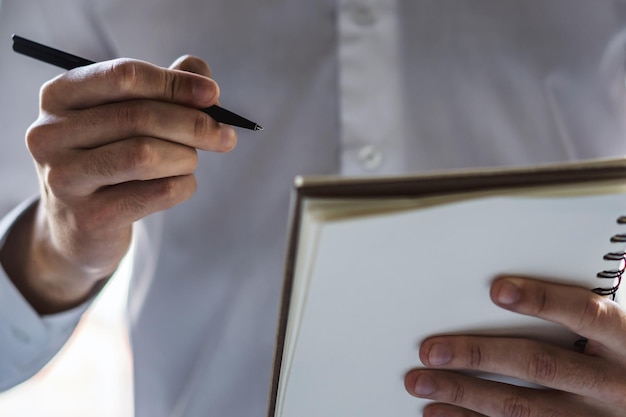 Man schrijft staand met een pen in dagboek in een zonnig kantoorbedrijf en onderwijsconcept Close-up