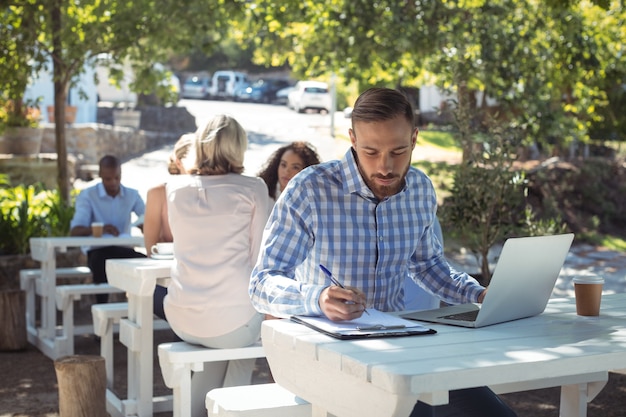 Man schrijven op klembord tijdens het gebruik van laptop