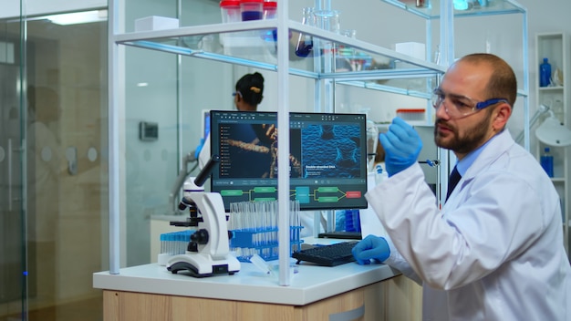 현대 실험실에서 Pc로 백신 개발 작업을 하는 남자 과학자. 과학 연구를 위한 첨단 화학 도구를 사용하여 의료 실험실에서 바이러스 진화를 조사하는 다민족 팀.