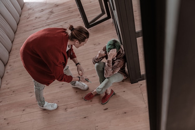 Man screaming. Green-haired woman sitting on floor and aggressive blonde-haired man screaming at her