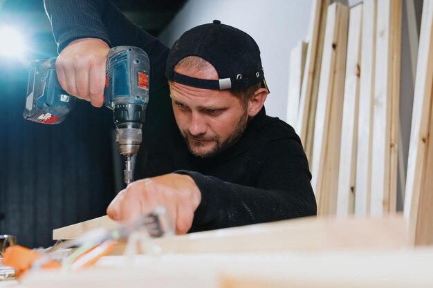 A man screws a screw into the board using an electric screwdriver Repair of wood products