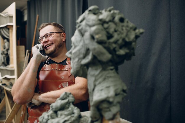 Фото Мужчина-скульптор создает скульптуру бюста из глины, человеческую женщину и звонит клиенту на мобильный телефон