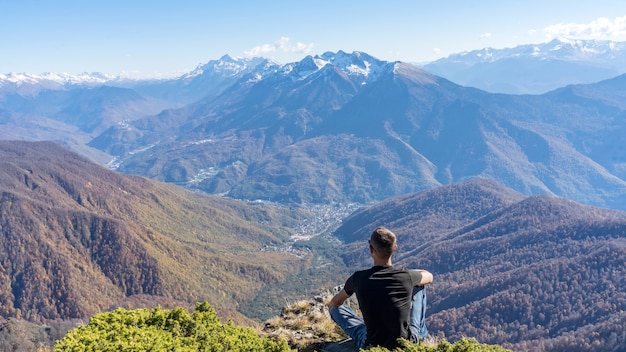 Man seats on the peak of Achisho mountain and looks on Krasnaya Polyana, winter in Sochi, Russia.