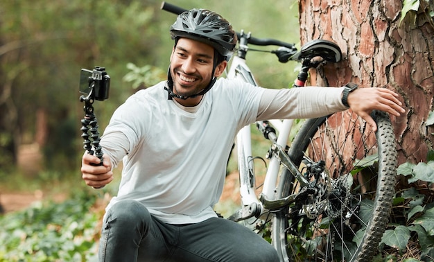 Man selfie en fiets door bomen bos en glimlach voor training gezondheid en buitenavontuur met webblog Influencer man fietsen en fietsen met livestream profielfoto en post op sociale media