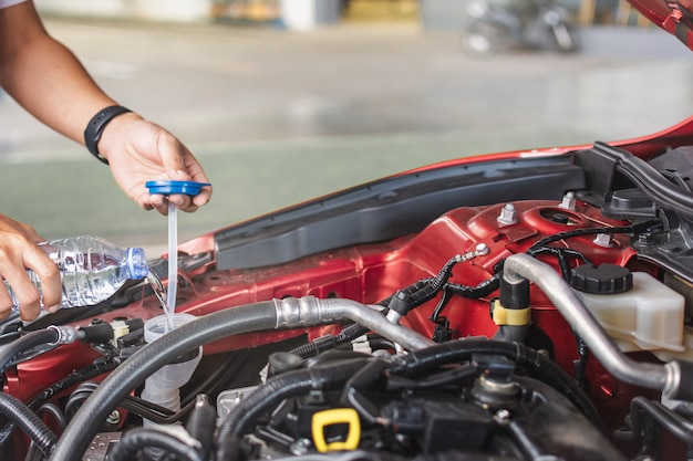 Man service monteur onderhoud inspectie service onderhoud auto Motor controleren met vulwater water toevoegen aan de ruitenwisserwagen in garage