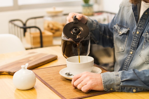 テーブルの上の白いカップでフィルターコーヒーを提供する男