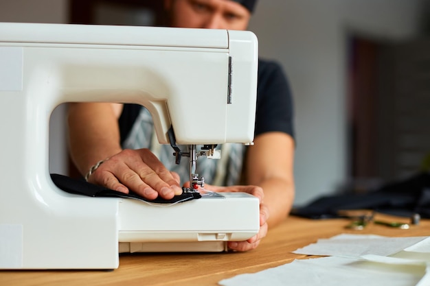 男はミシンで洋服を縫うアトリエ繊維産業で縫製をしている男性の仕立て屋趣味のワークスペース小さなビジネス作成プロセスDIY針子の職場