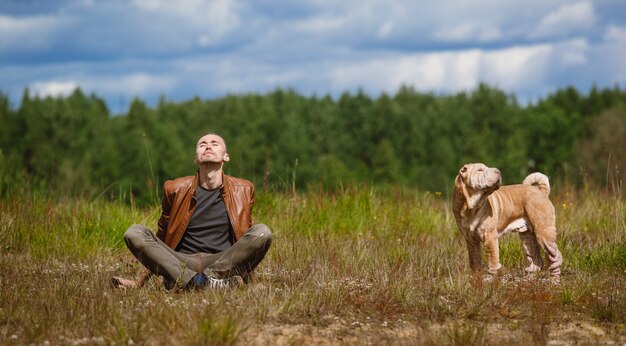 Man and a shar pei breed dog sitting on the ground