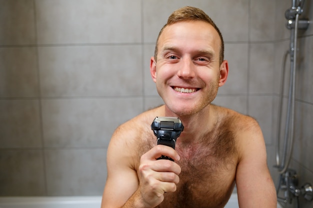 男は鏡の前で電気かみそりで顔を剃る。皮膚の炎症。入浴手順