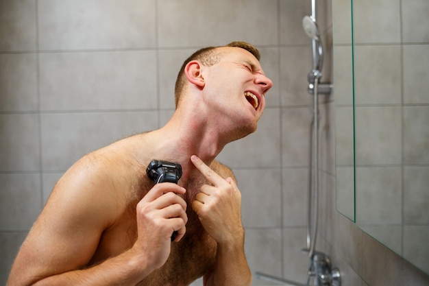 한 남자가 거울 앞에서 전기 면도기로 얼굴을 면도하고 있다. 피부 발진. 목욕 절차