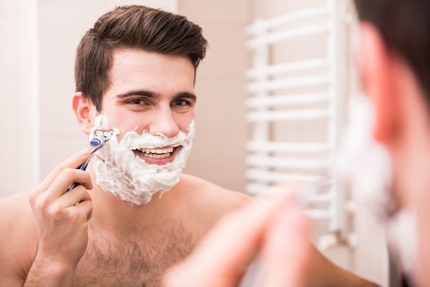 Man shaves and smiles in the bathroom.