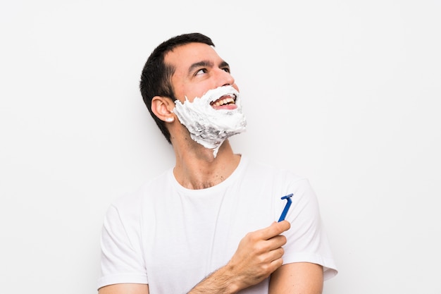 Man shaving his beard over isolated white looking up while smiling