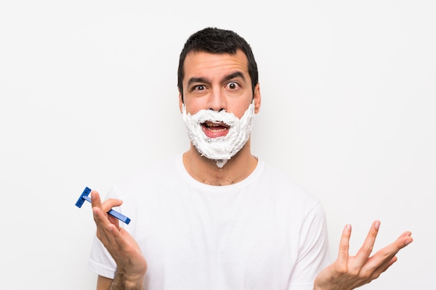 Man shaving his beard over isolated white wall making doubts gesture