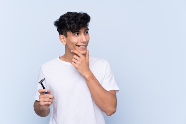 Man shaving his beard over isolated white wall thinking an idea and looking side