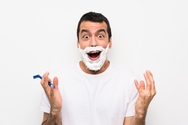 Man shaving his beard over isolated white wall with shocked facial expression