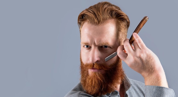 Man shaving with barber blade isolated on grey background with copy space barber man shaving with blade man in barber studio man hold barber blade for shaving