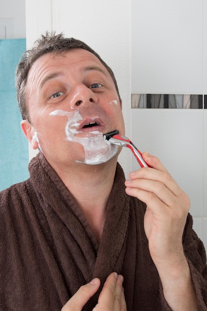 Мужчина бреется лезвием бритвы и кремом для бритья в ванной