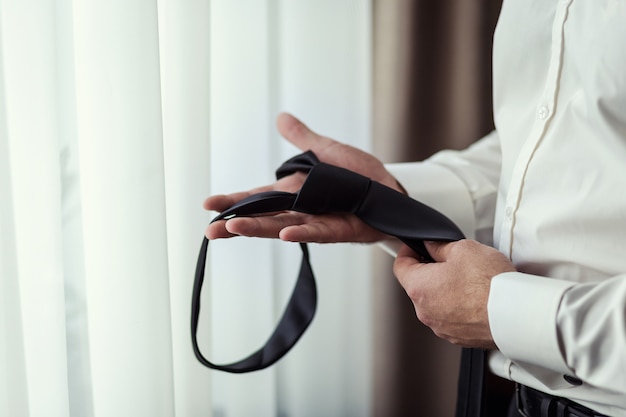 man in shirt dressing up and adjusting tie on neck at home