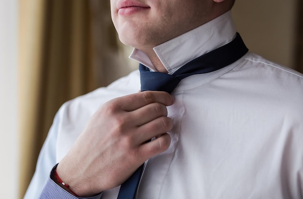 мужчина в рубашке наряжается и поправляет галстук на шее дома