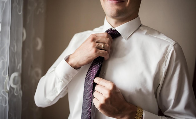 Man in shirt dressing up and adjusting tie on neck at home