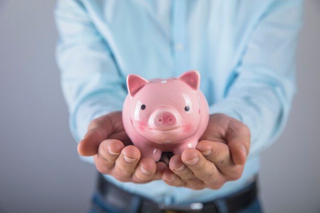 A man in a shirt holds a piggy bank in his hand